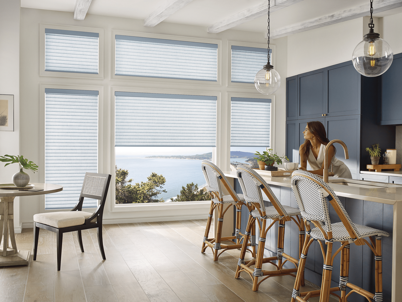 A woman in a kitchen gazing out large picture windows with Sonnette PowerView Shades.